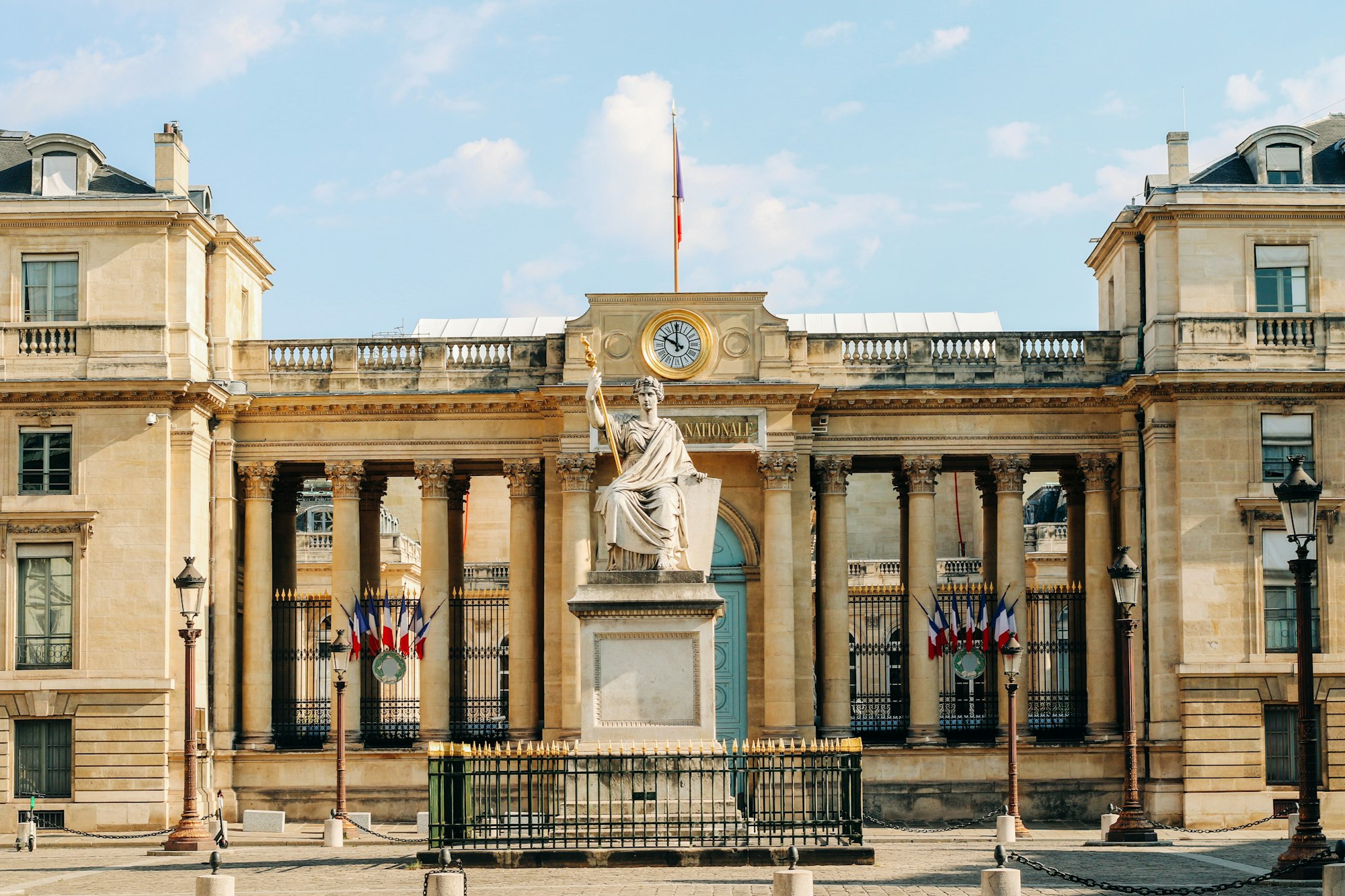photo-1604595818635-a840f9028d56 The white columned facade and statue of the French parliament building in Paris under a cloudy sky.