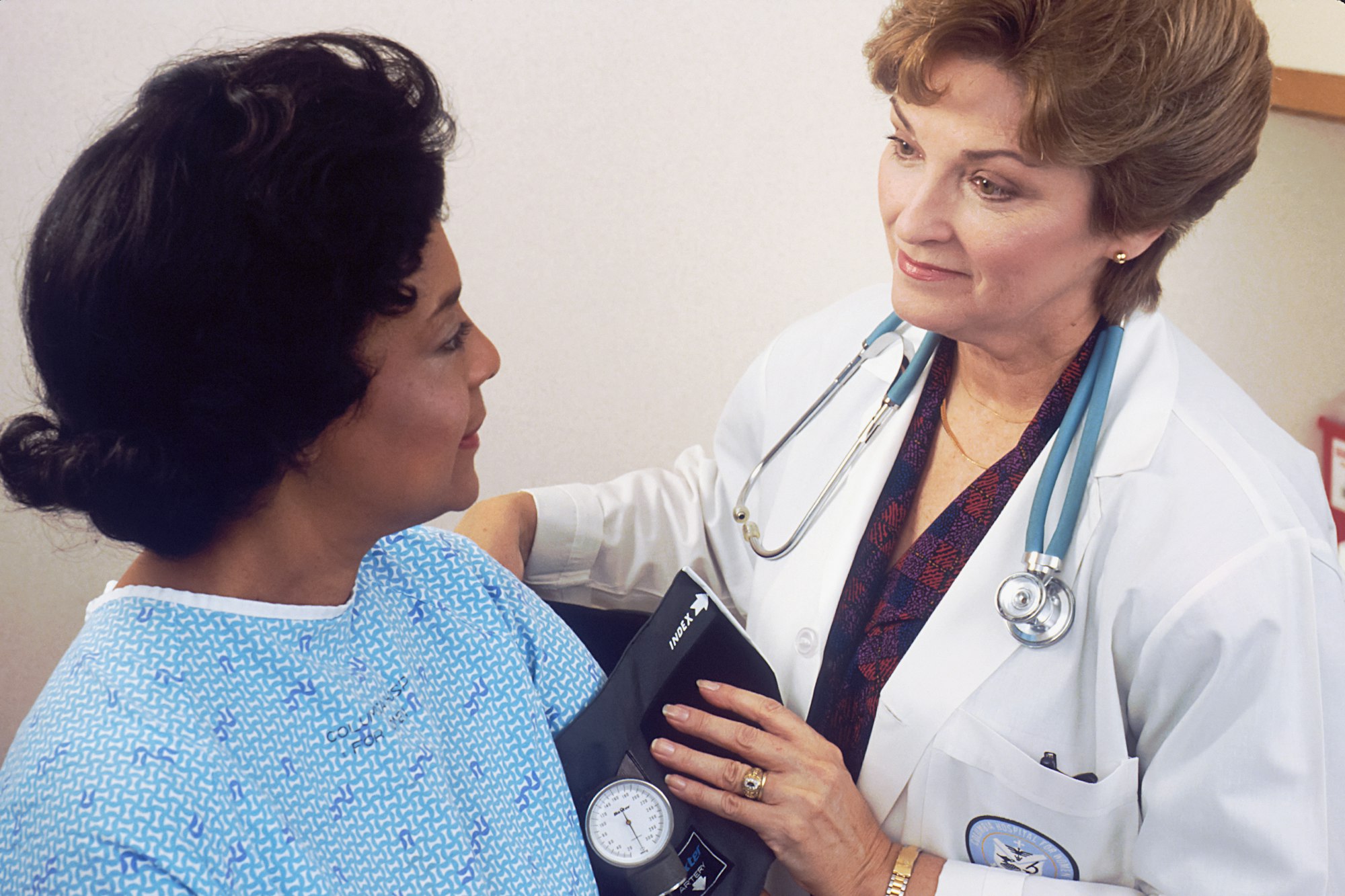 photo-1631558556874-1d127211f574 A doctor with a stethoscope takes a woman's blood pressure while they talk.