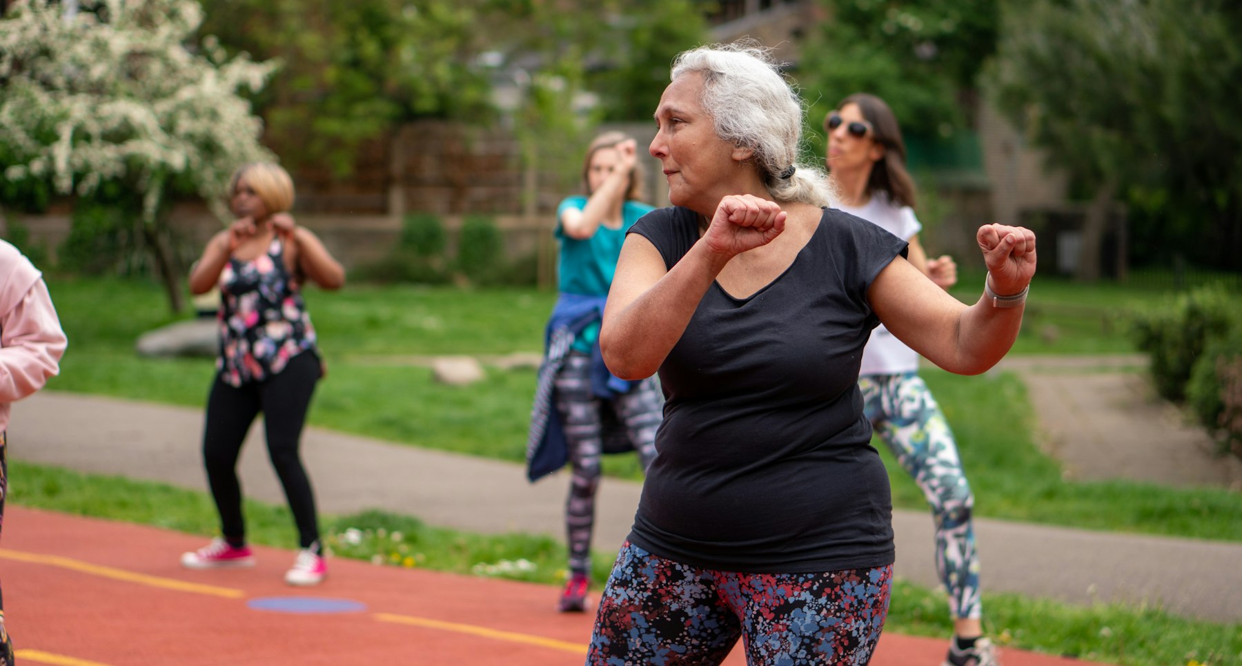 photo-1658314755561-389d5660ee54 An older woman exercises with others at an outdoor fitness class