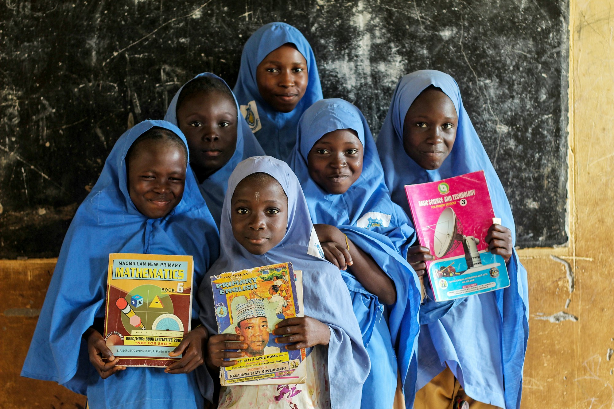 photo-1666281269793-da06484657e8 A group of young women in Africa hold up books in a classroom.