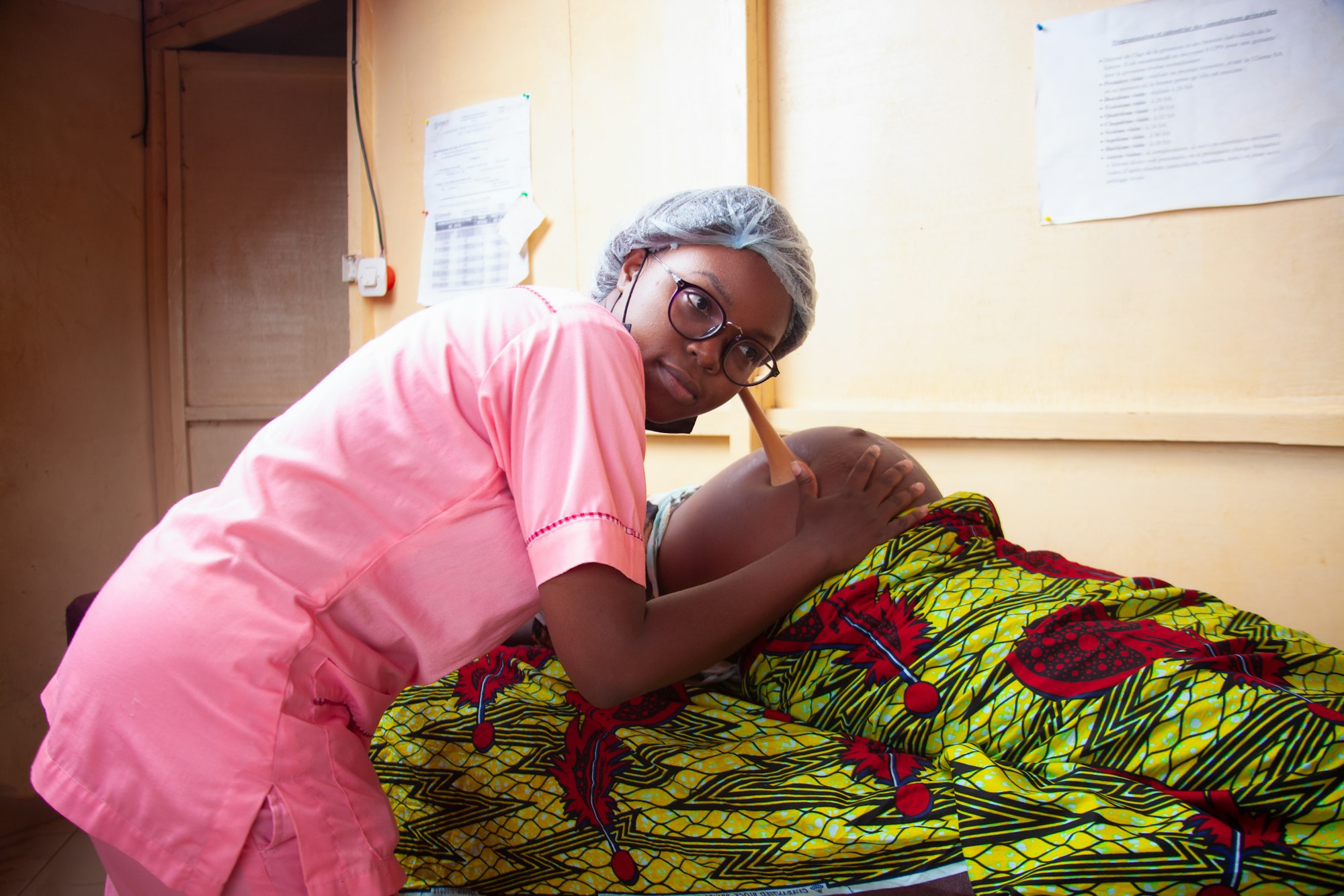 photo-1677682693104-bc4758db3b45 A midwife sits with a pregnant woman in a green and yellow dress.