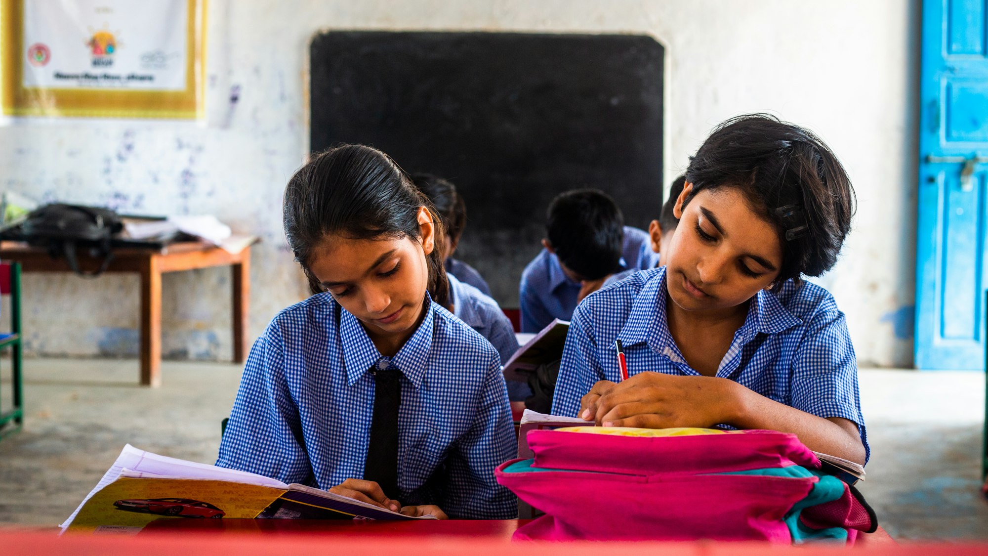 photo-1692269725911-87697c558be1 Two girls in India sit together at a desk in a classroom.