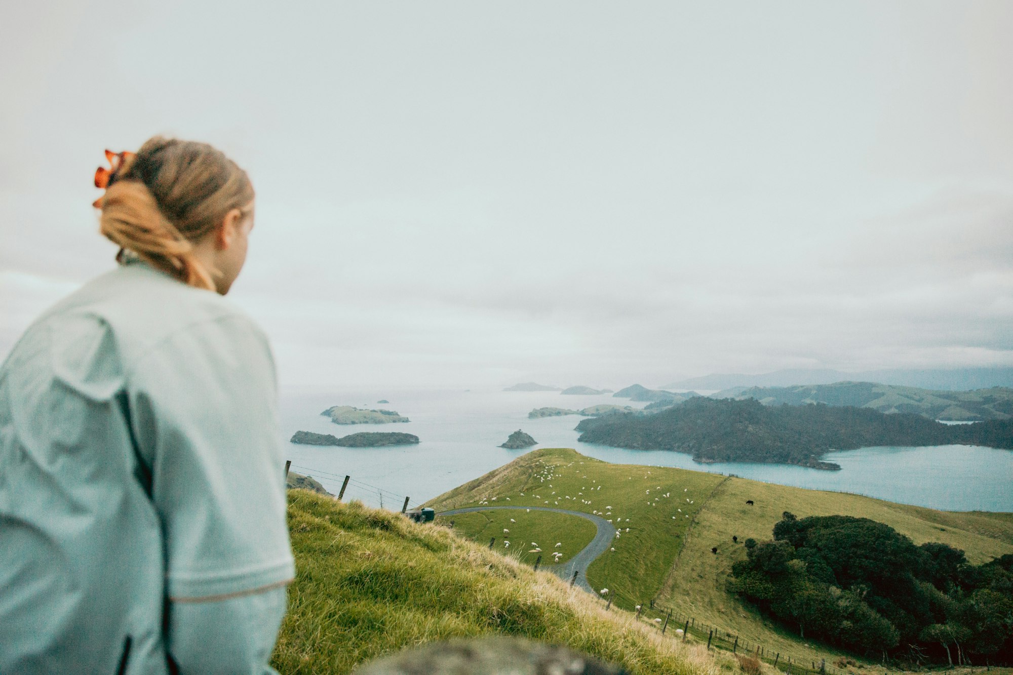 photo-1717739189475-6e41efc3588d A woman standing on a green hillside in the New Zealand countryside.