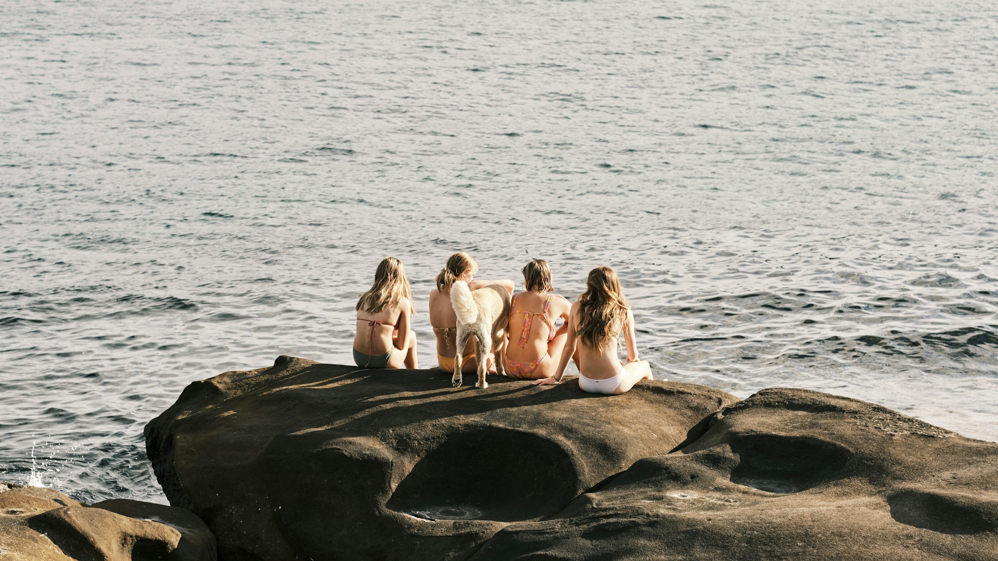 photo-1720445561763-1963b75cef08 A group of women sit together on a rock beside the ocean at Malabar Beach in New South Wales, Australia.