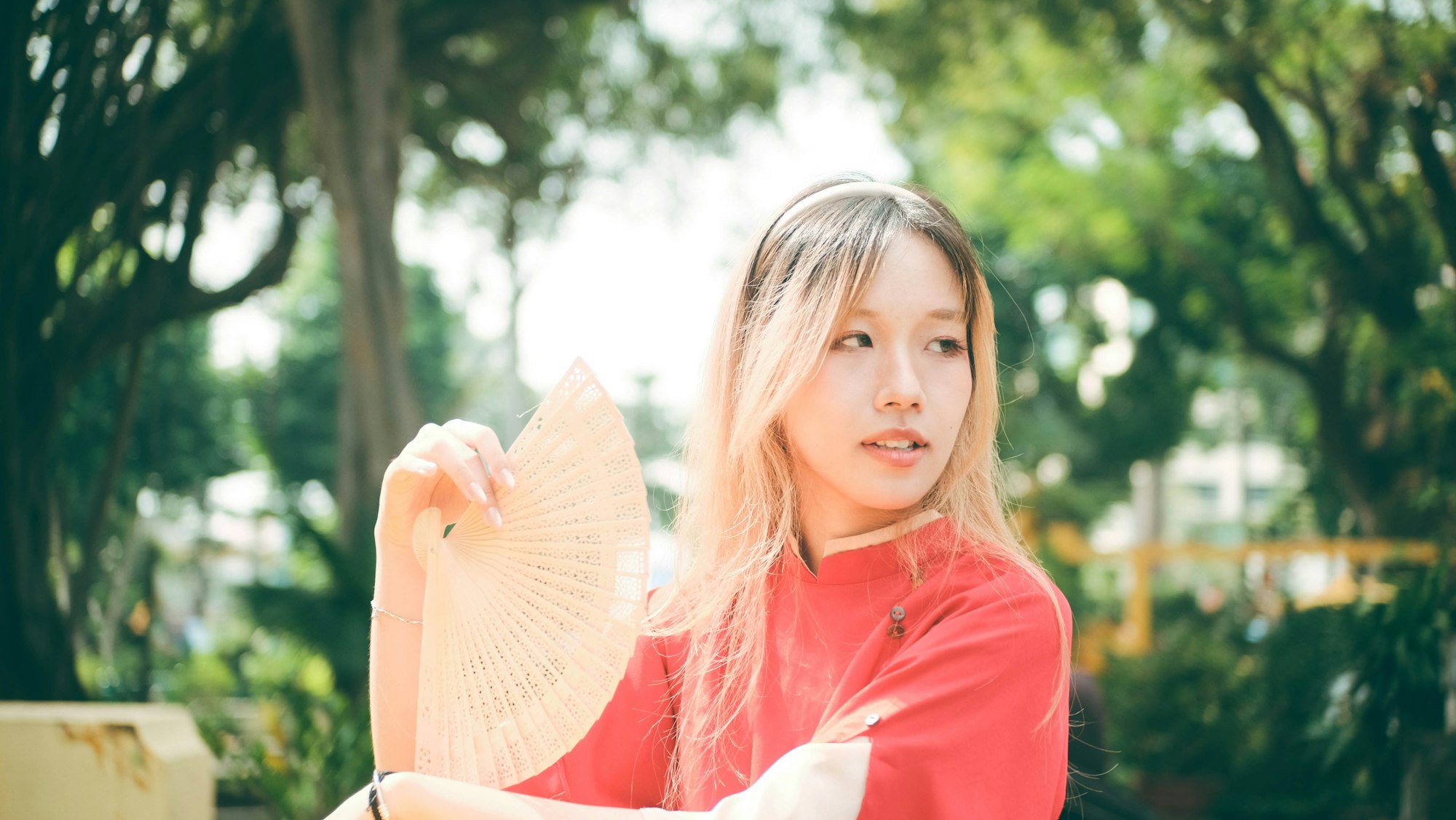photo-1736350987550-584e94444410 A woman sits on a bench holding a hand fan.