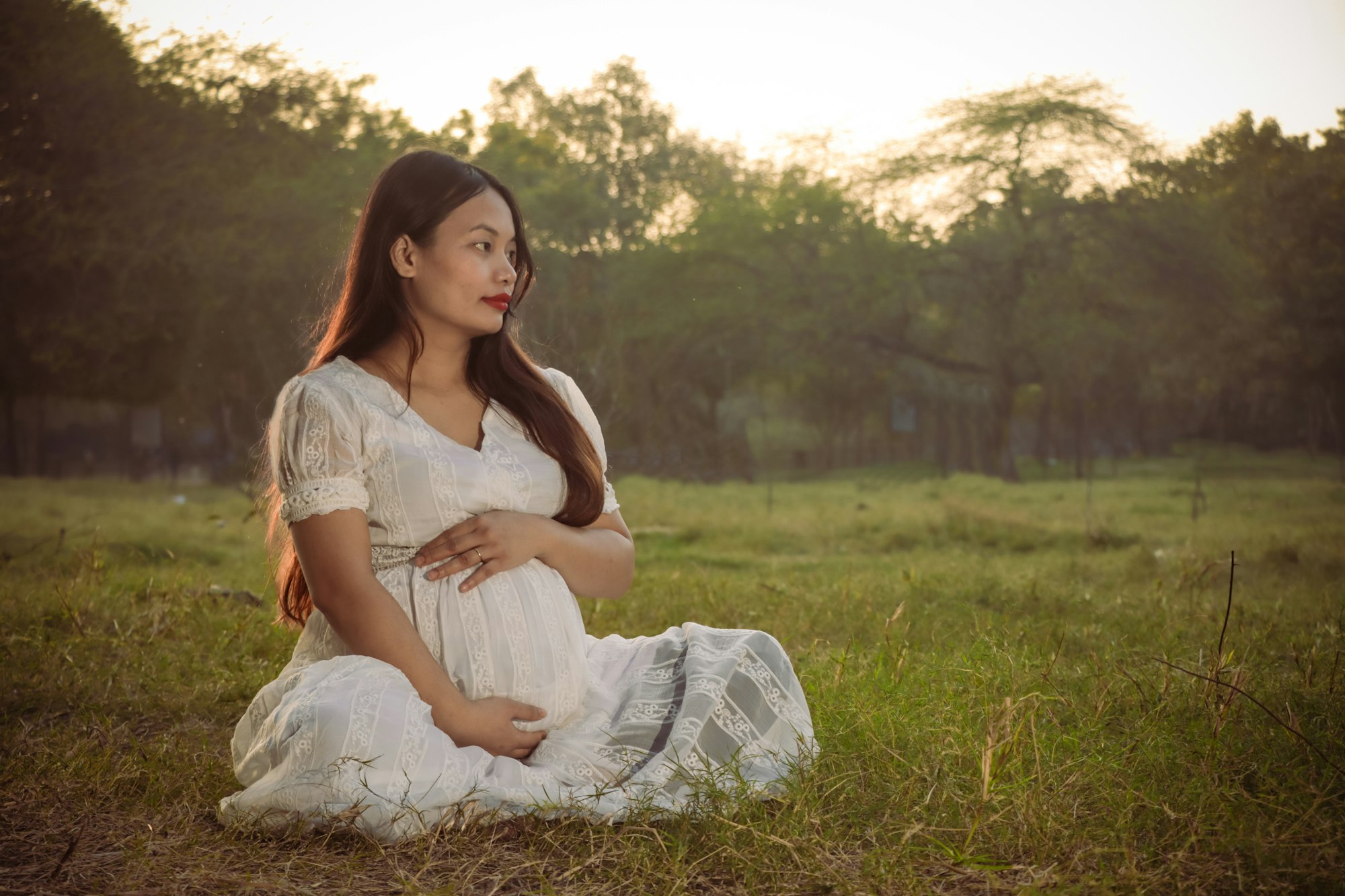 photo-1739287376717-91c8f1fe89c1 A pregnant woman sits in a field in India as the sun sets.