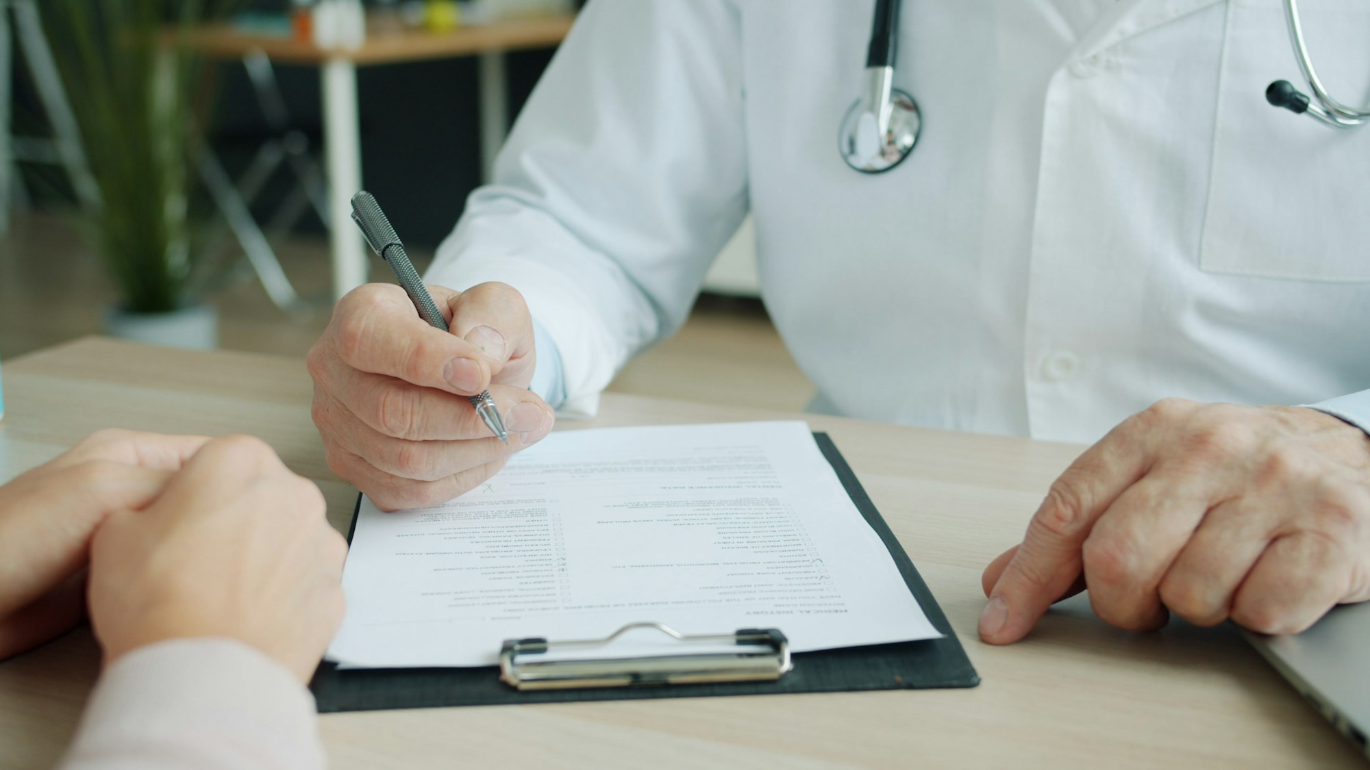 photo-1758691461990-03b49d969495 A doctor writes notes on a patient's chart during a clinic appointment.