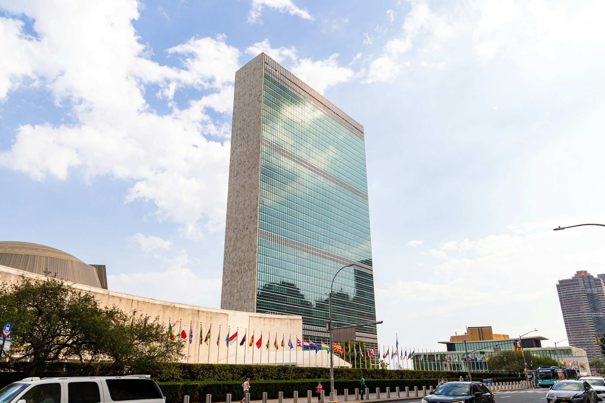 photo-1761301643520-49c1ee626e72 Flags flying outside the United Nations headquarters building in New York.