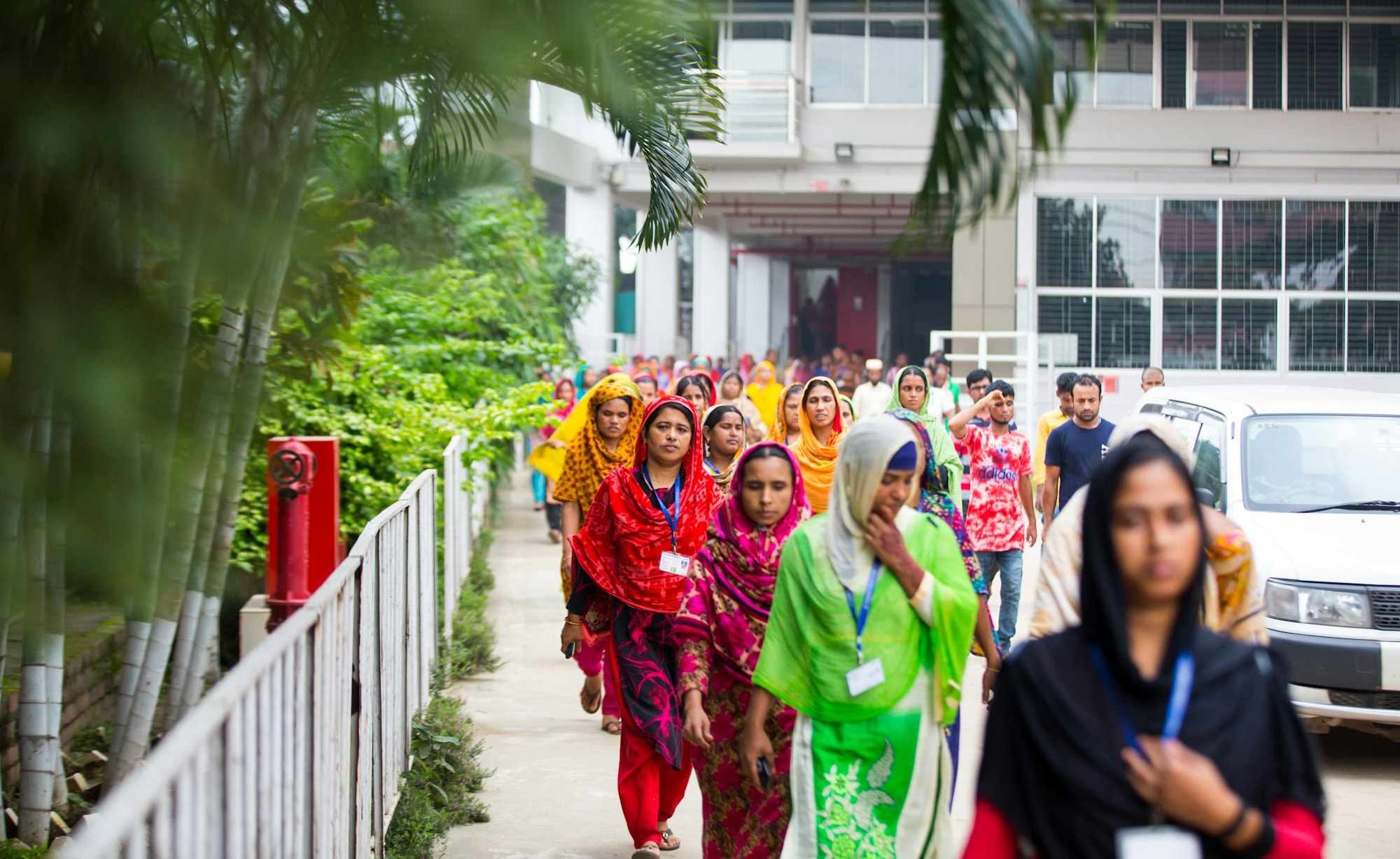 photo-1780899695191-2bcb7f28fda8 Women garment workers in colourful clothing walk through a factory compound in Bangladesh.