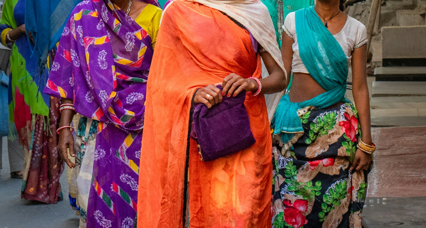 photo-1793280503084-b29136847043 A group of women in colourful saris walk together down a narrow street in Udaipur, India.